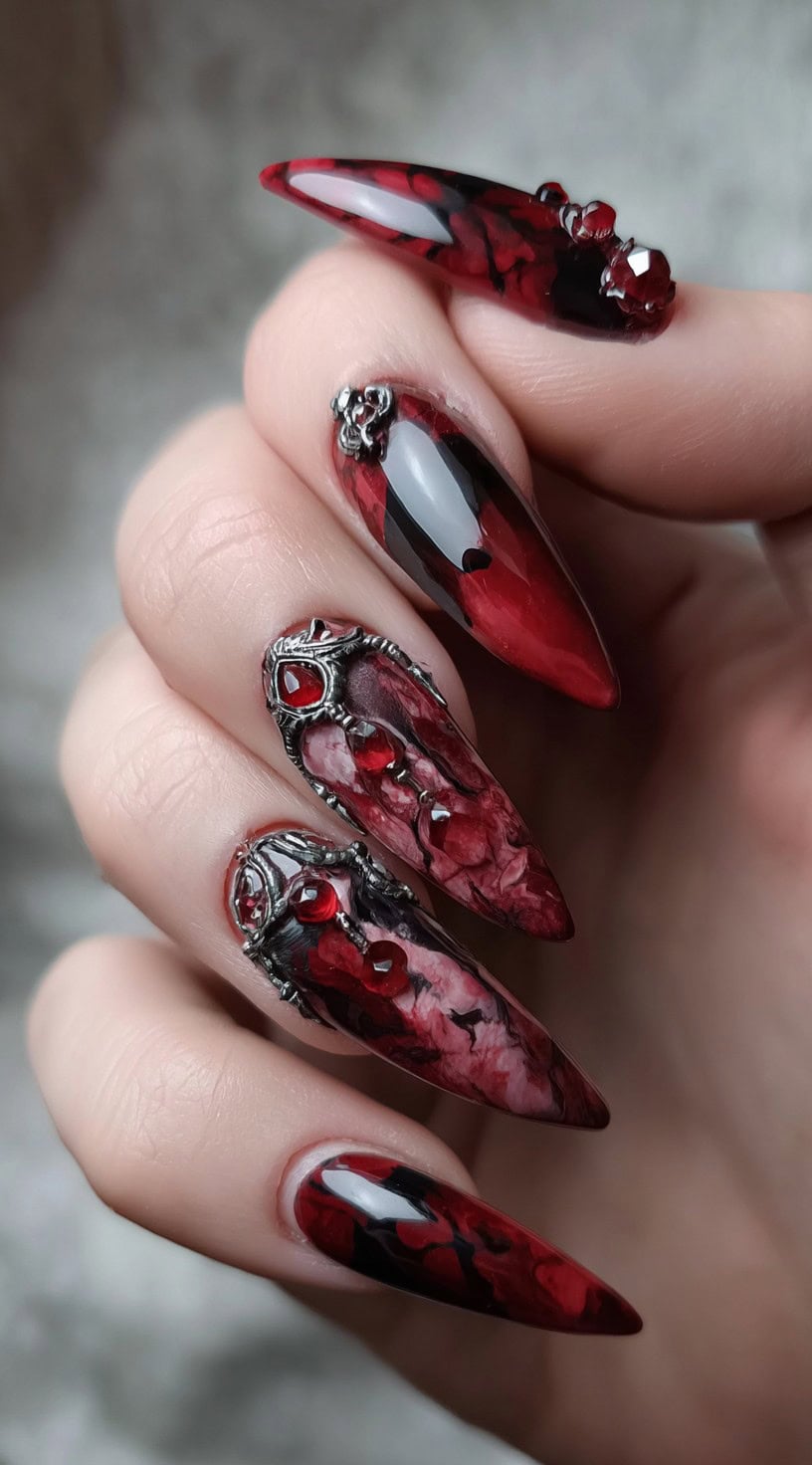 Stiletto nails layered with red and black marbling, silver gothic embellishments, and deep red jewels.