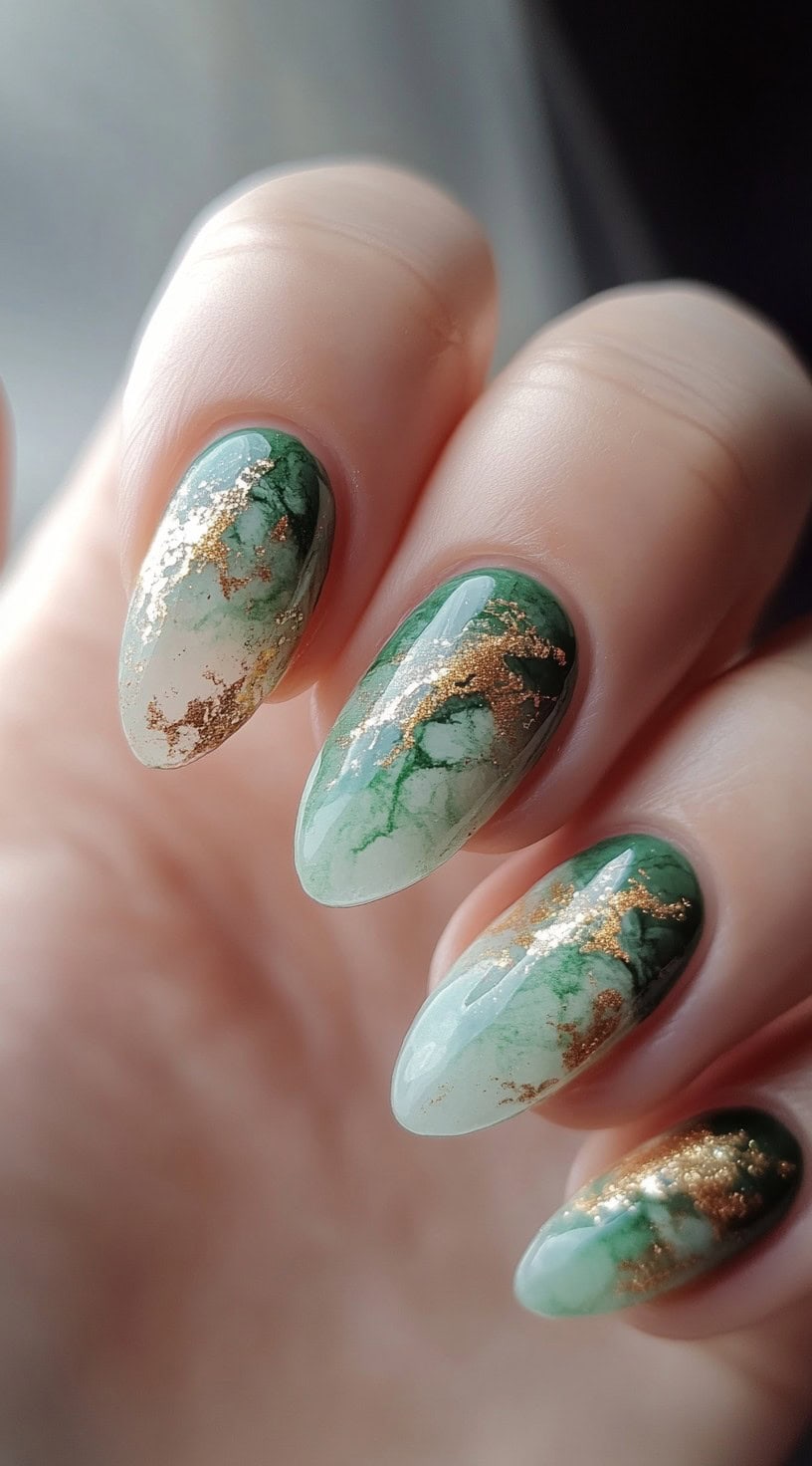 A set of almond-shaped nails with a soft green and white marble effect, enhanced by delicate gold veining for a luxurious, natural stone-inspired design.