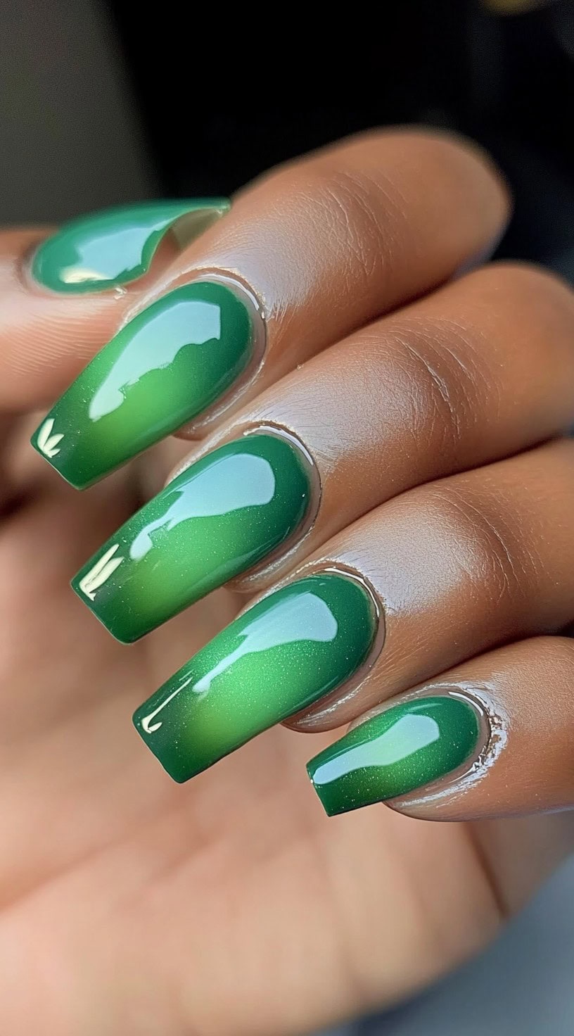 A hand with medium-length coffin-shaped nails featuring a vibrant green aura effect with a high-gloss top coat.