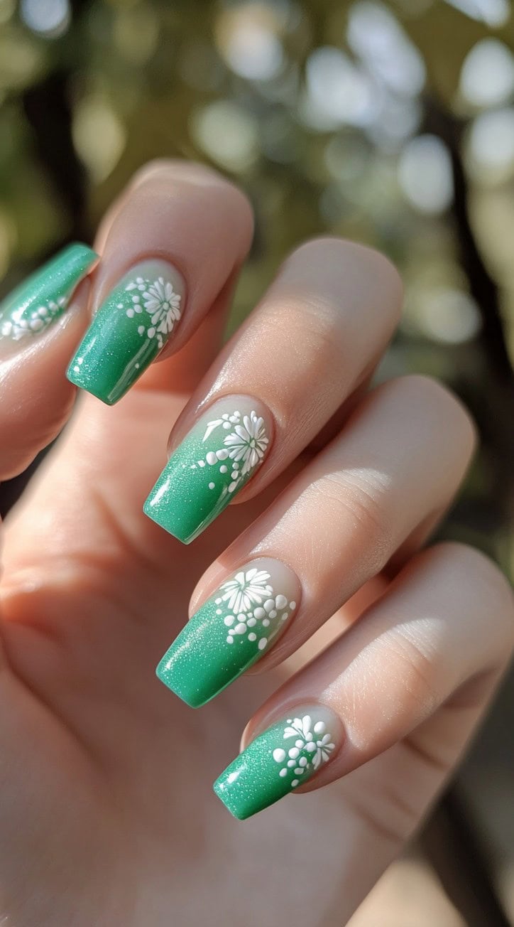 A set of square-shaped nails with a soft green ombre base, featuring hand-painted white floral accents for a delicate and feminine look.