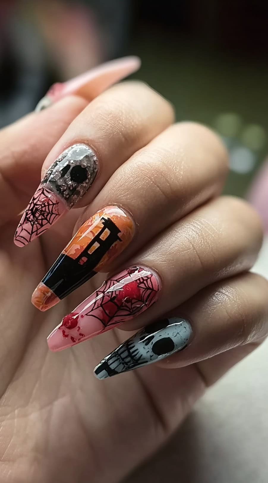 A hand with long coffin-shaped nails featuring a haunted house, spider webs, blood splatter, and skull art.