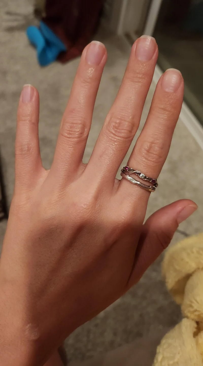 A hand with unpolished nails wearing stacked silver rings, resting against a cozy indoor background.