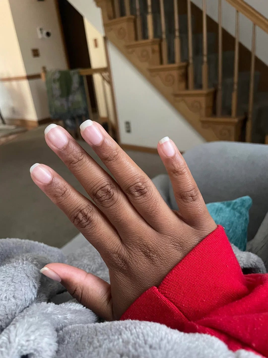 Hand with clean, healthy natural nails and rounded tips resting on a cozy blanket indoors.
