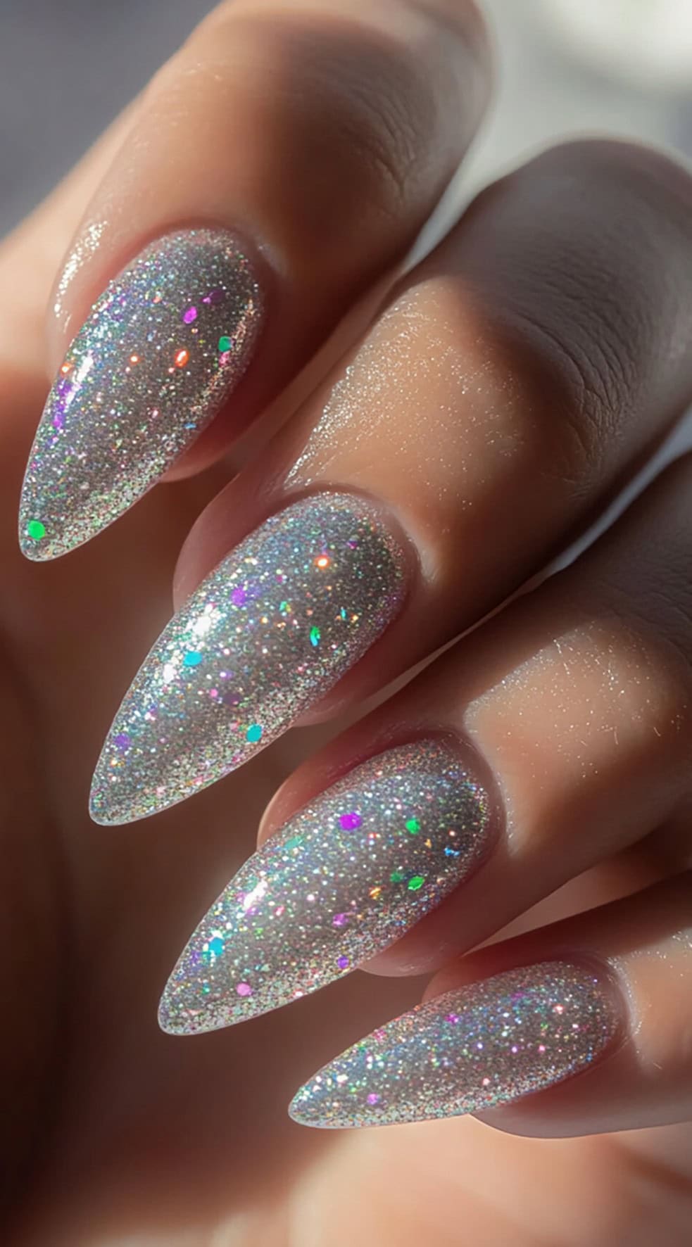 A set of long, stiletto-shaped nails coated in a dazzling holographic glitter polish that shifts colors under the light.