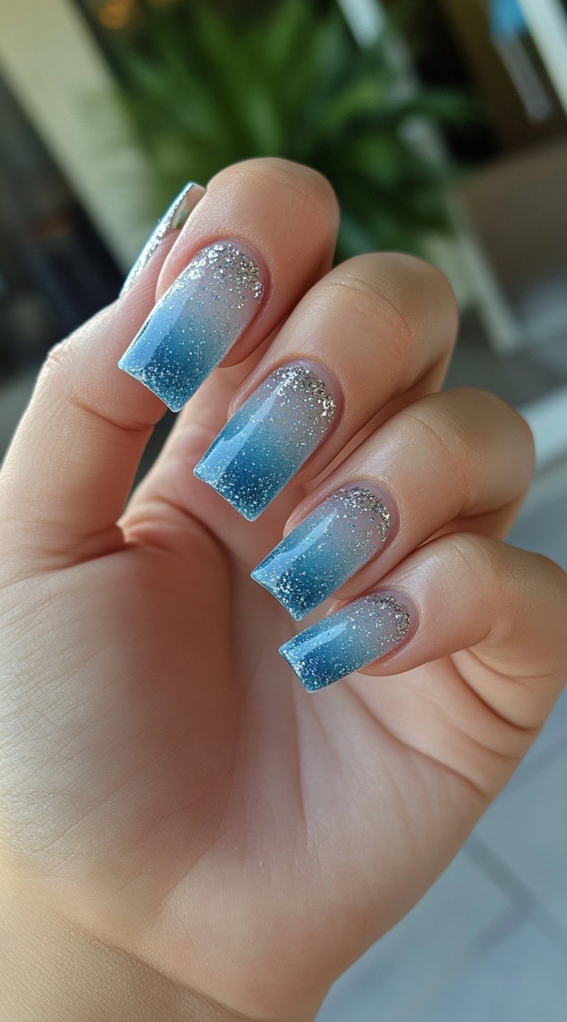 Coffin-shaped nails with a sheer to icy blue ombre and dense silver glitter near the cuticle.