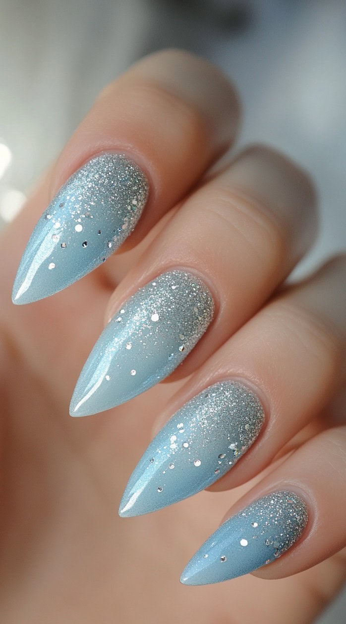 Long stiletto-shaped nails transitioning from a soft icy blue to a sparkling silver glitter ombre.