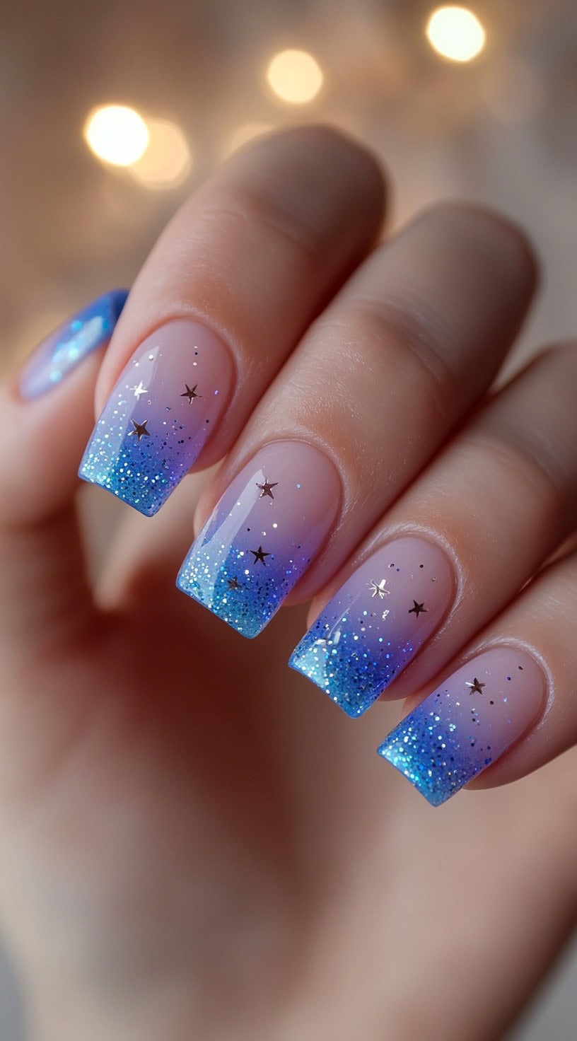 Square nails with clear to blue ombre glitter tips and scattered silver star decals.