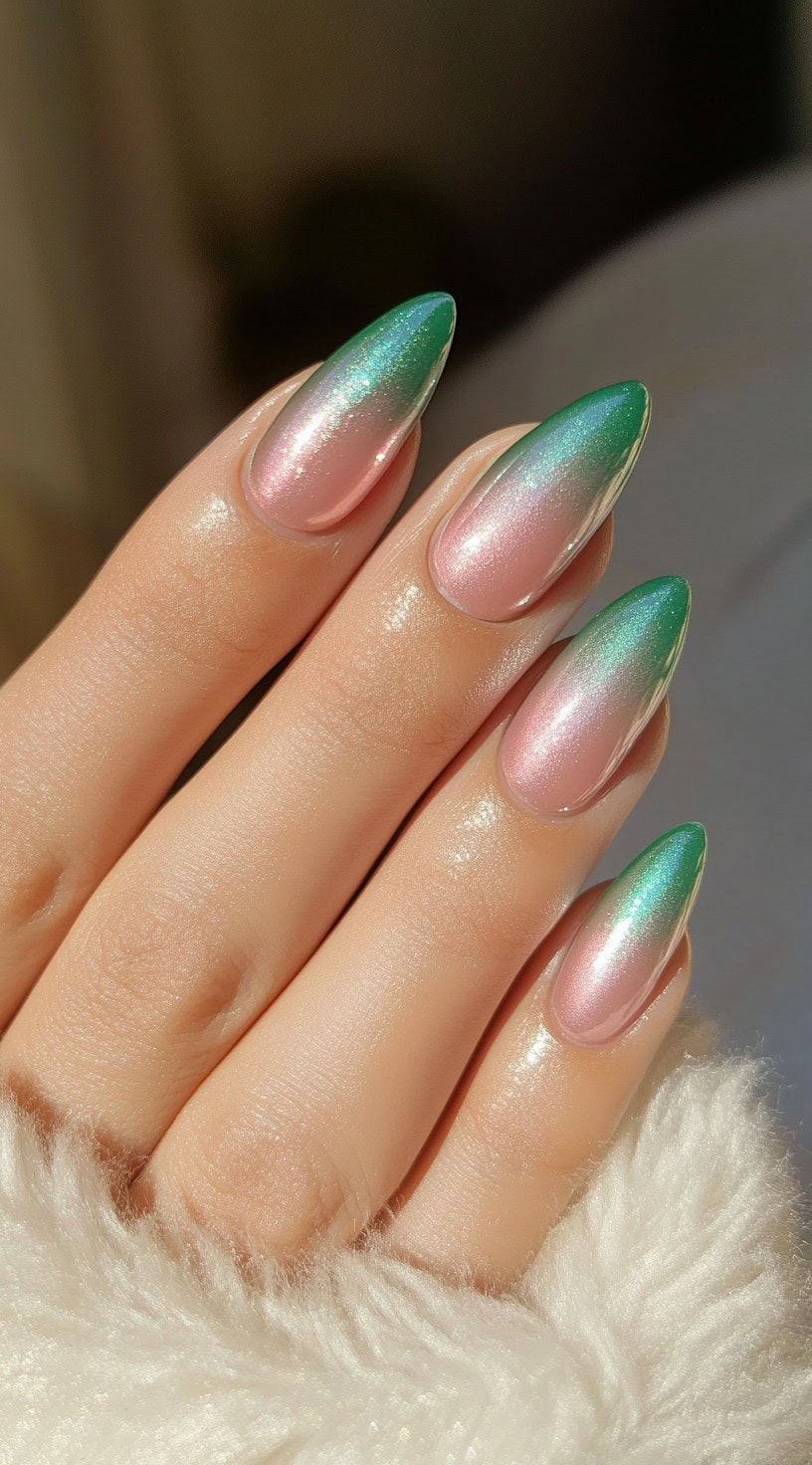 A hand with almond-shaped nails featuring a pink to green ombre design with a chrome, iridescent finish.
