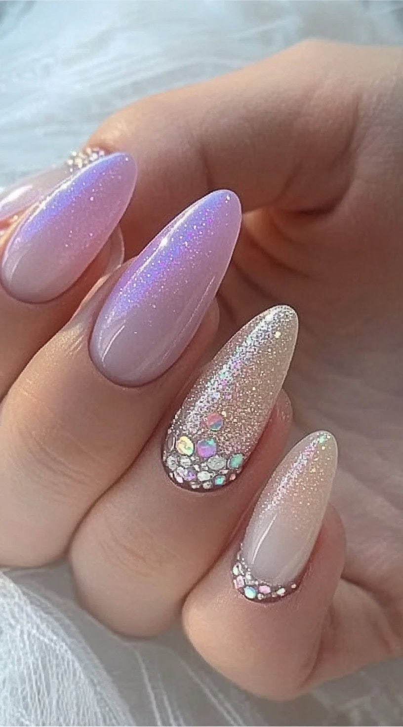 A set of long almond-shaped nails featuring a dreamy iridescent ombré effect with glittery tips and crystal embellishments.