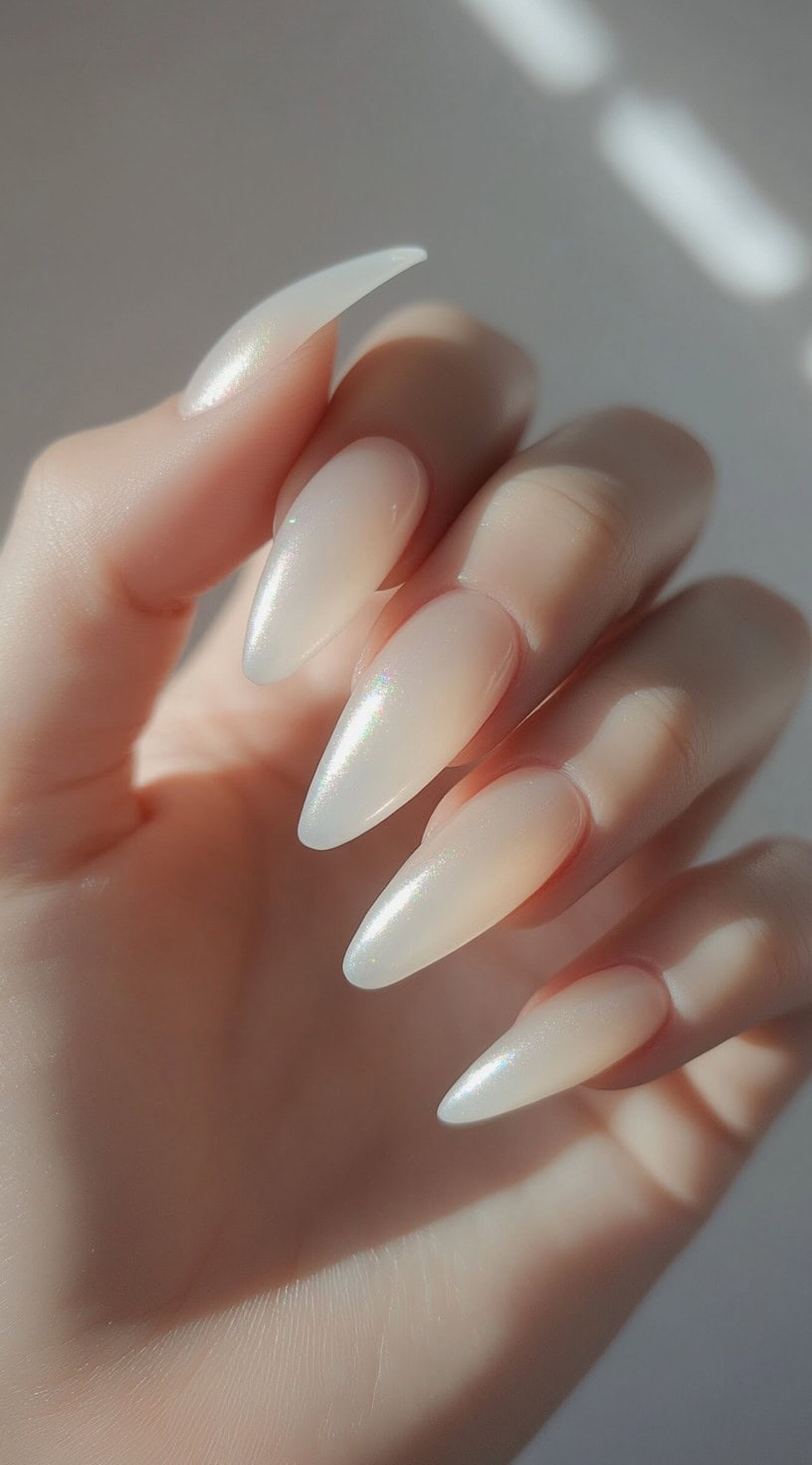 A hand with almond-shaped nails featuring a sheer nude base with a subtle iridescent shimmer.