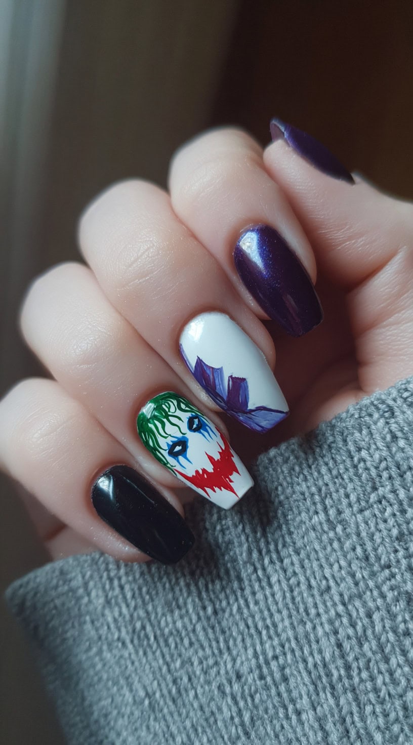 A set of nails with a mix of black and purple polish, featuring an accent nail with a Joker face and purple suit detail.