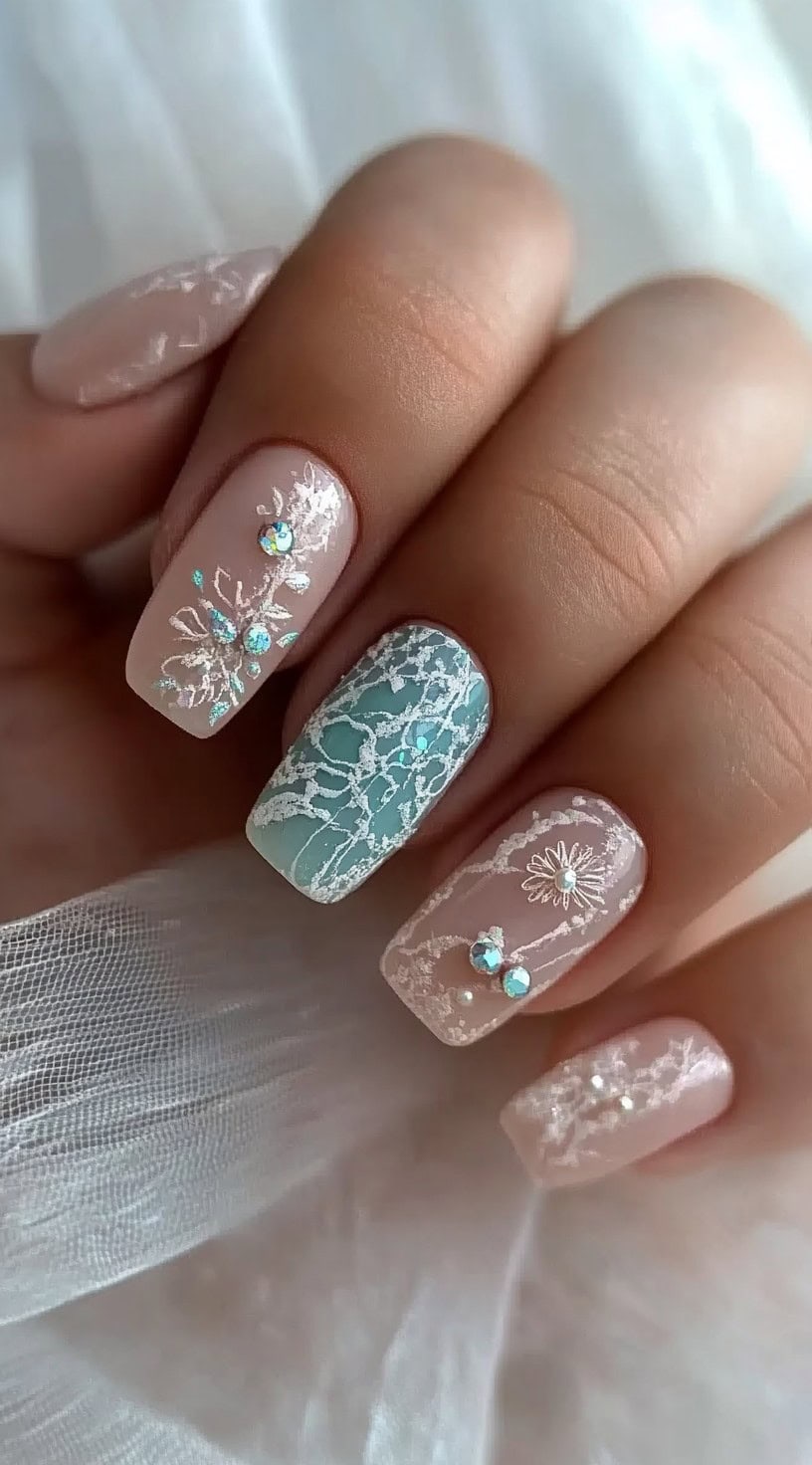 Square-shaped nails featuring a nude and soft teal base, decorated with intricate lace patterns and tiny rhinestone accents."