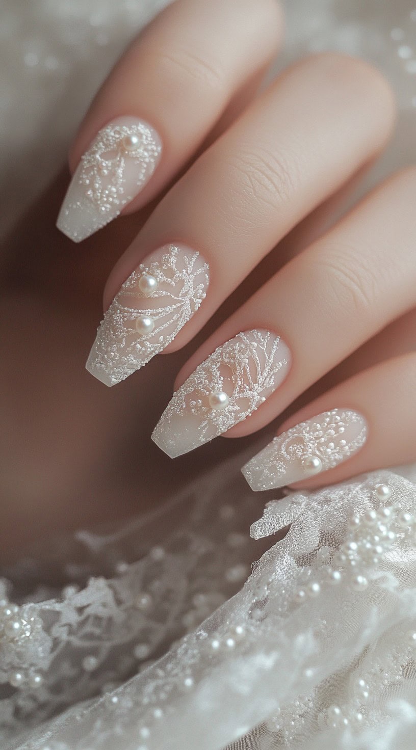 Coffin-shaped nails with sheer white lace detailing, pearl accents, and intricate beaded textures for a bridal-inspired effect.