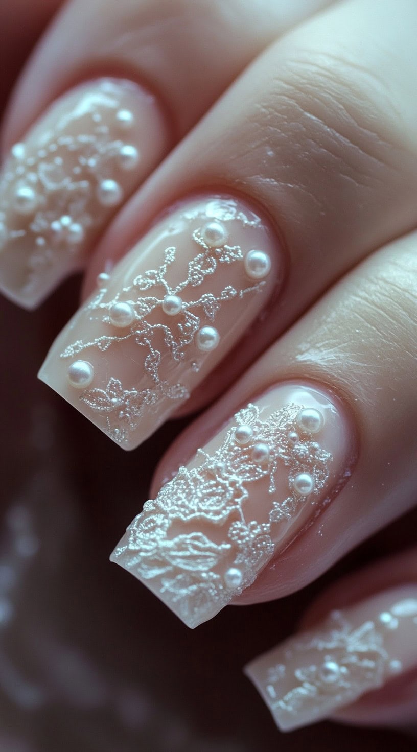 A close-up of square nails with an intricate lace-like design made from fine white detailing and pearl embellishments.