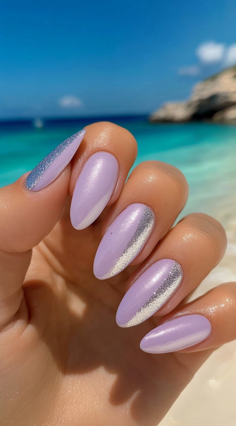 Almond-shaped nails with a soft lavender base and glitter accents in silver and lilac, glistening under the beach sun.