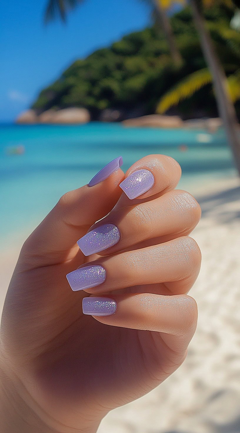 Square-shaped nails in a delicate lavender shade with subtle glitter accents, glowing against a tropical beach backdrop.