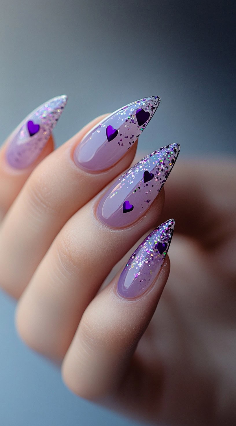 Stiletto-shaped lavender nails with a glitter gradient and purple heart-shaped confetti.
