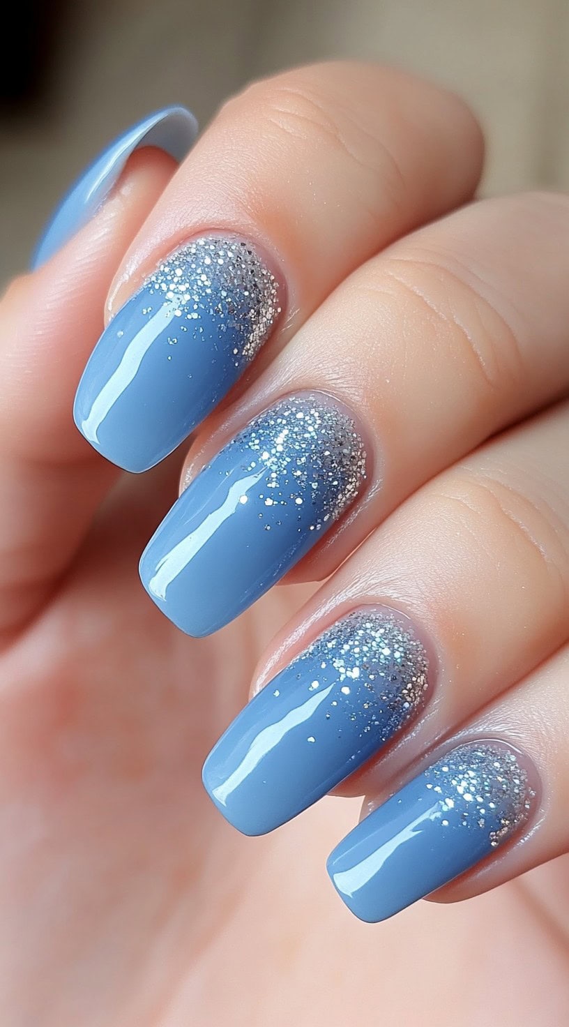 Square nails painted light blue with a glitter ombre at the base.