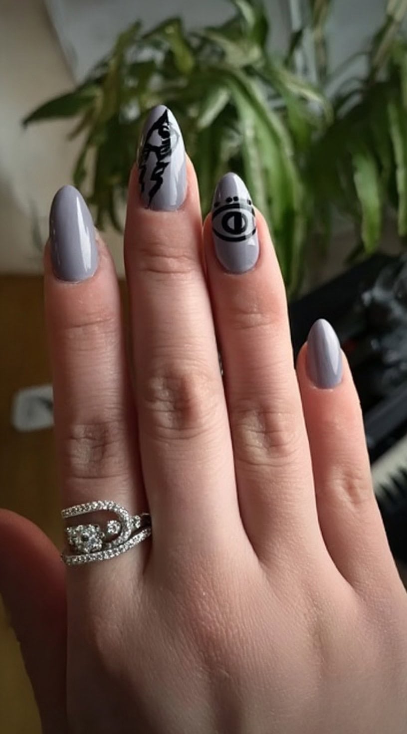 A hand with glossy light grey nails decorated with black abstract witchy symbols like an eye and lightning bolt.