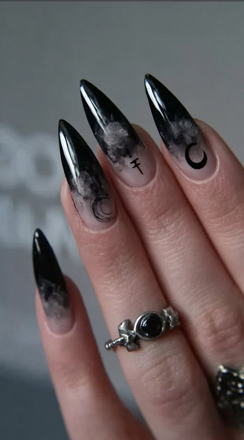 Glossy stiletto nails with a foggy black ombré design and subtle occult symbols like crescent moons and ancient crosses.