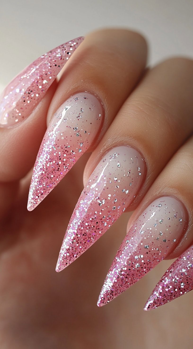 A close-up of long stiletto nails featuring a soft pink and white ombre with silver glitter sprinkled throughout.
