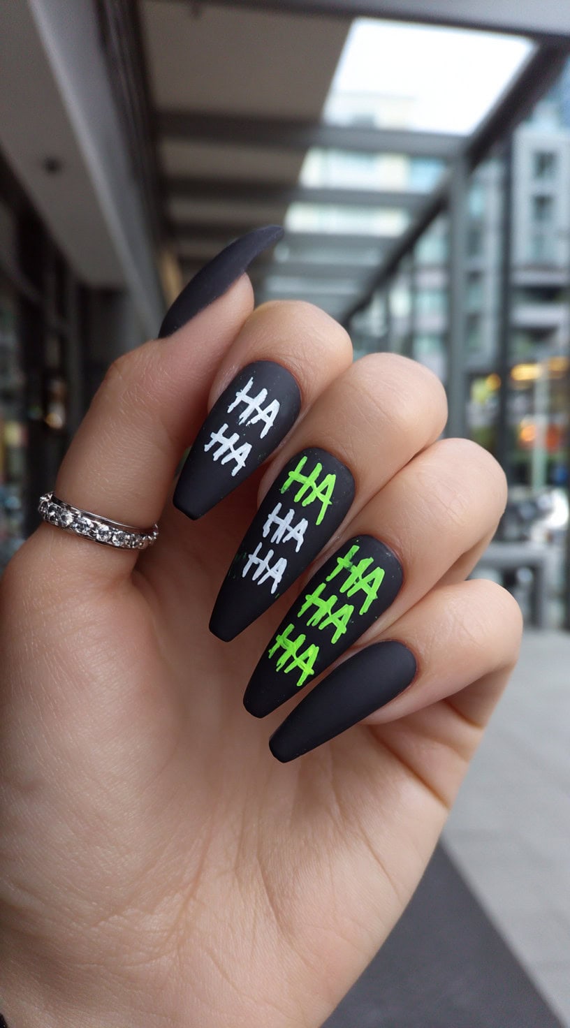 Long matte black coffin nails with neon green and white 'HA HA' laugh text painted on each nail.