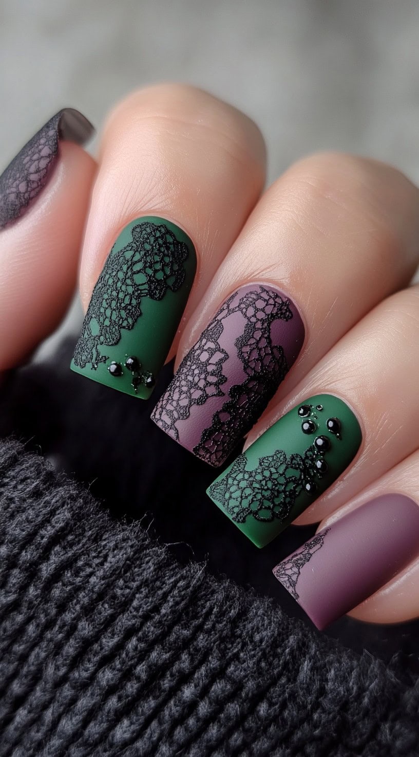 Hand with matte purple and green square nails adorned with black lace patterns and glossy black beads.