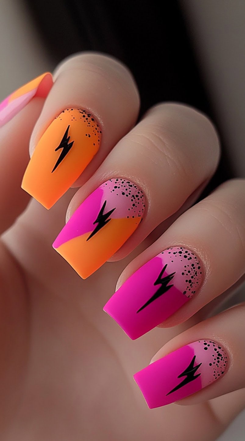 Squoval-shaped matte nails in hot pink and orange with black lightning bolt decals and black splatter accents.