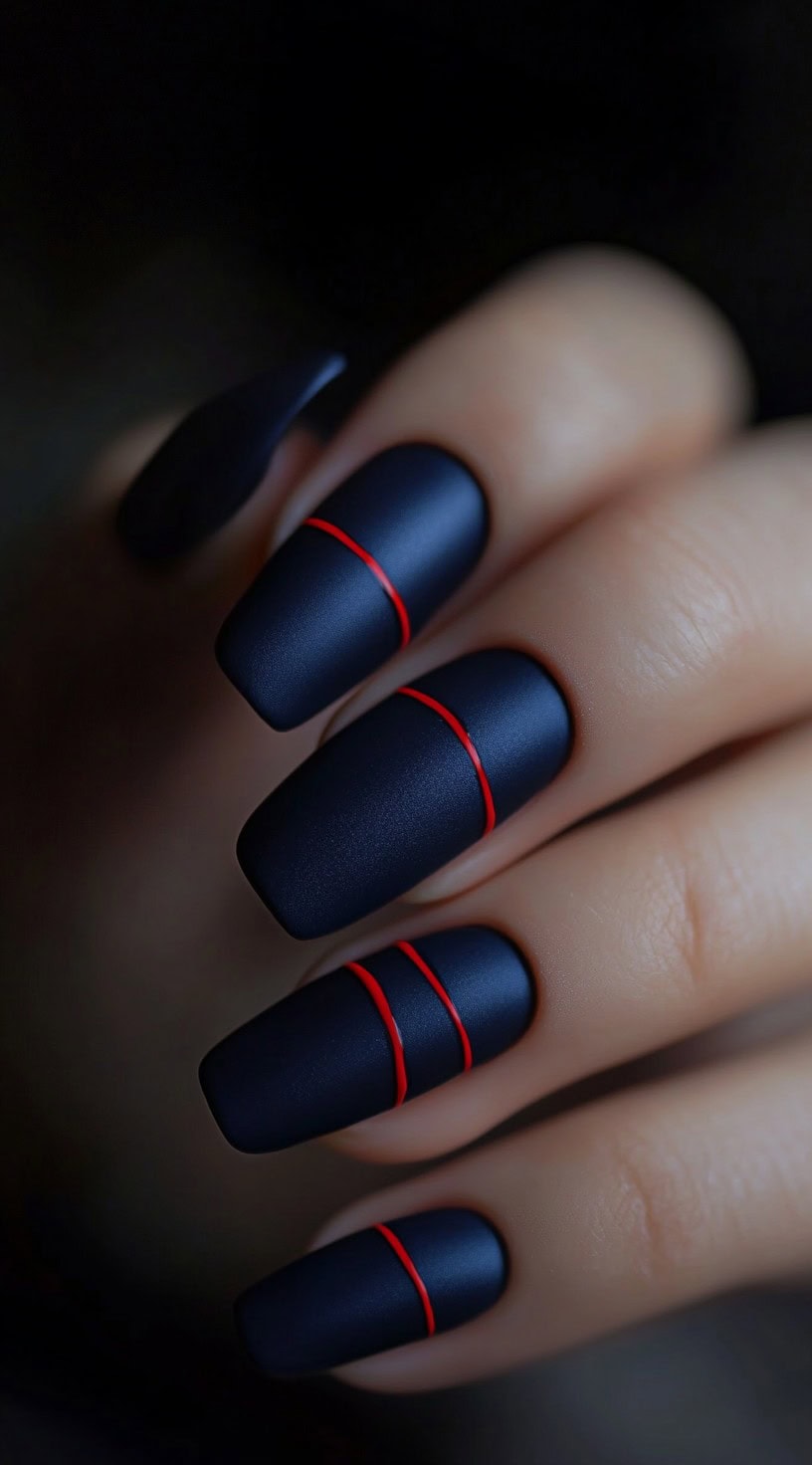 A hand featuring square-shaped nails painted in deep matte navy blue, each adorned with a single thin red line for a sleek, minimalist effect.