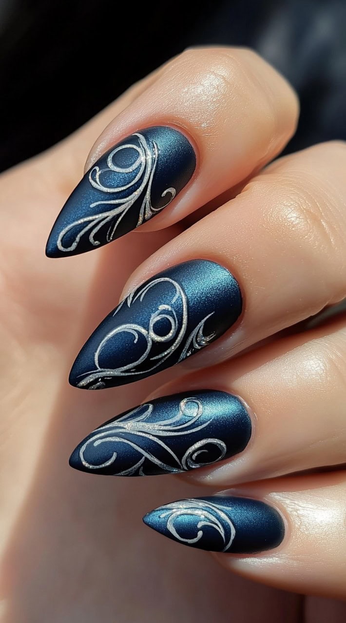 Matte navy blue stiletto nails with intricate silver swirl detailing.