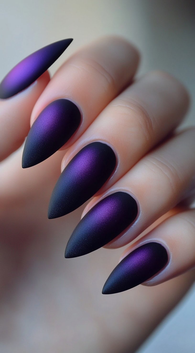A hand with long stiletto nails featuring a matte purple-to-black ombré design.