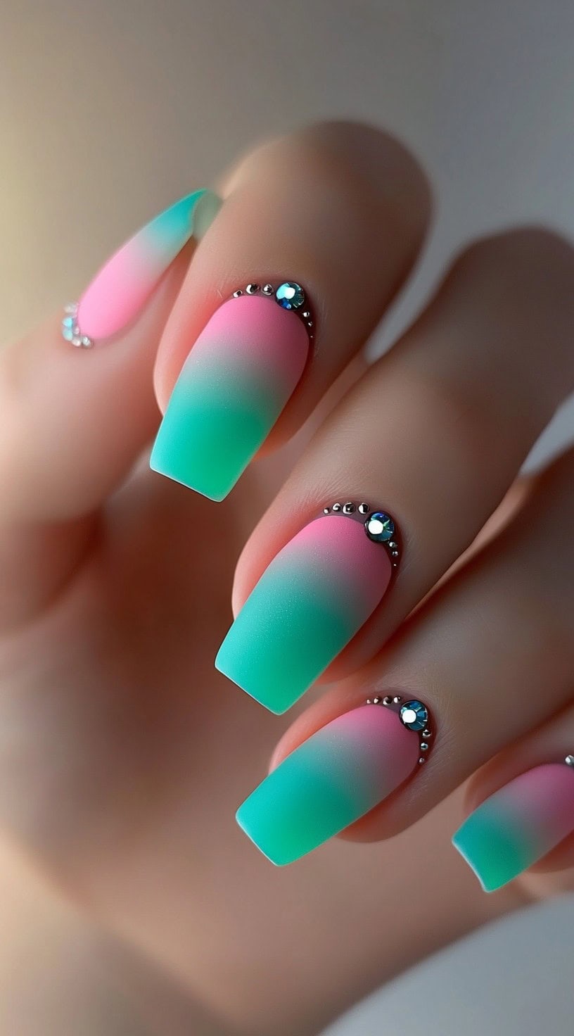 Square-shaped matte nails with a soft pink and green ombre base, decorated with silver and teal rhinestones at the cuticles.