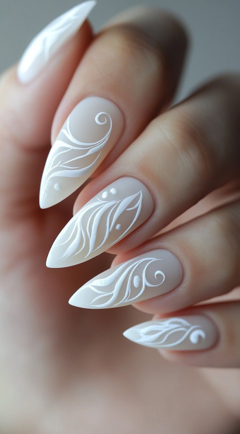 Five matte white almond-shaped nails decorated with fine white scroll and leaf-like detailing in a soft, ornamental style.