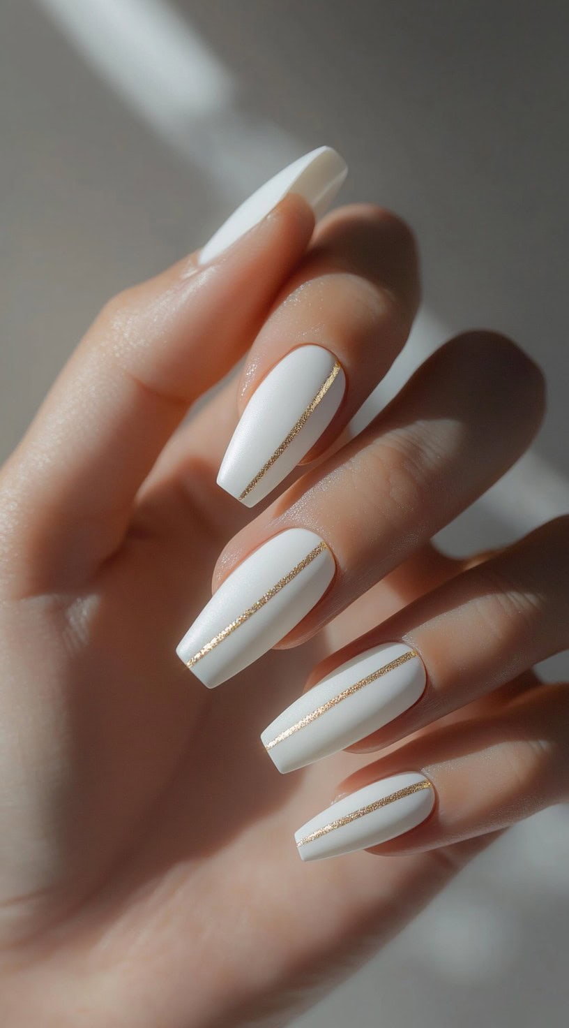 A set of long matte white square nails featuring thin, precise gold line accents running vertically down the center.