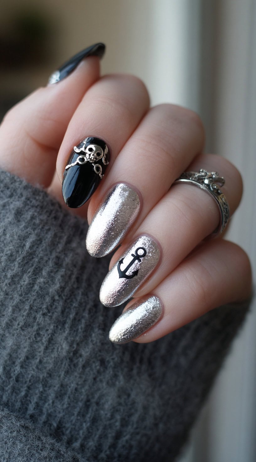 Shiny silver almond nails are paired with a black accent nail featuring a 3D skull charm and another with an anchor decal.