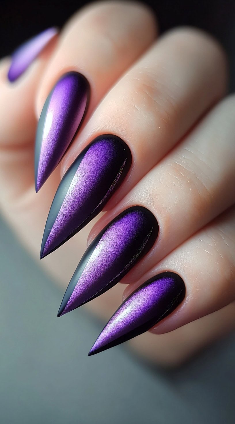 A hand with stiletto-shaped nails featuring a metallic purple chrome center that fades into soft matte black edges.