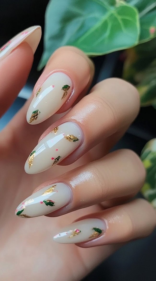 A set of almond-shaped nails with a translucent nude base, featuring delicate gold leaf flakes and tiny floral details.