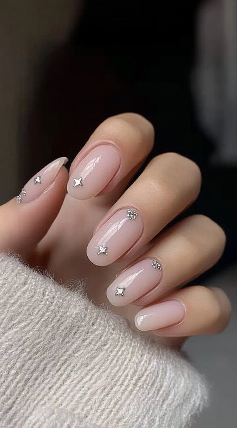 A close-up of a bride's hand with short, natural-looking almond nails featuring a sheer pink base with tiny silver star embellishments on select nails.