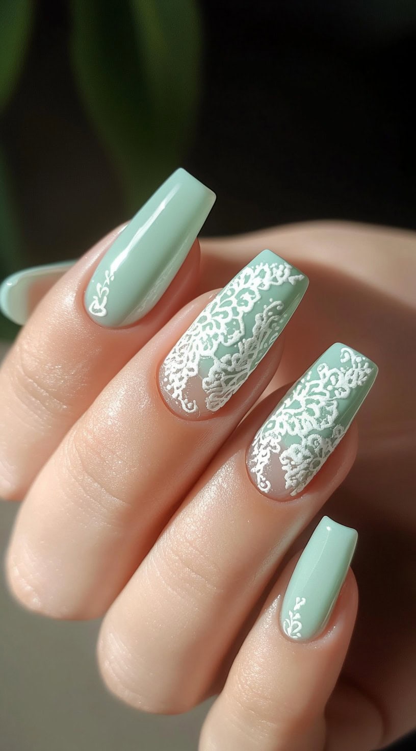 A set of square-shaped nails in a soft mint green shade, featuring intricate white lace detailing for a delicate, bridal-inspired look.