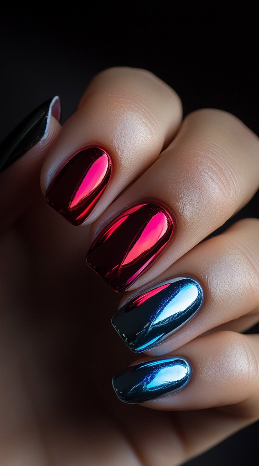 A hand featuring square-shaped nails with a high-shine mirror chrome finish, alternating between deep red and metallic blue.