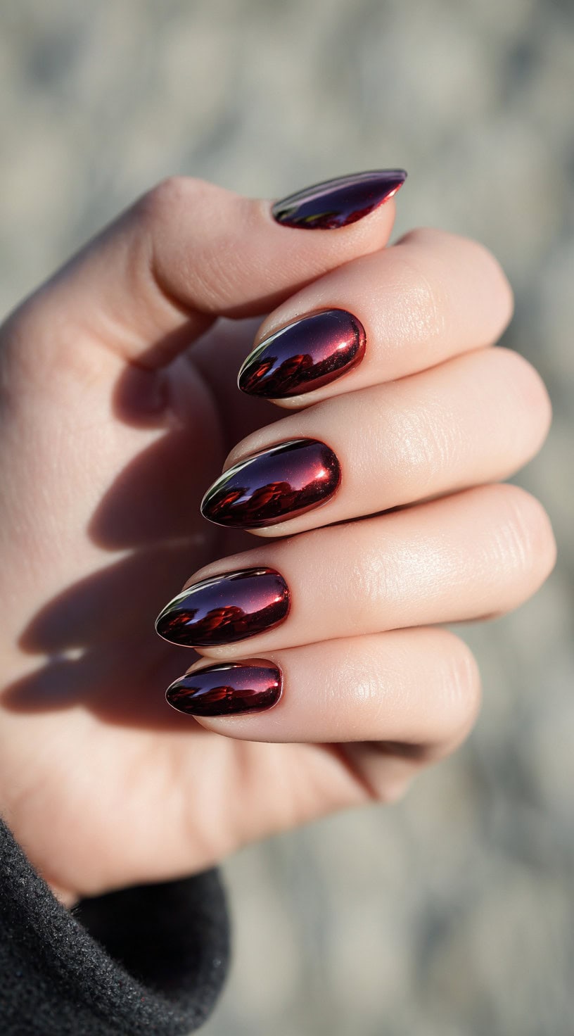 A hand with almond-shaped nails coated in a reflective wine red chrome finish.