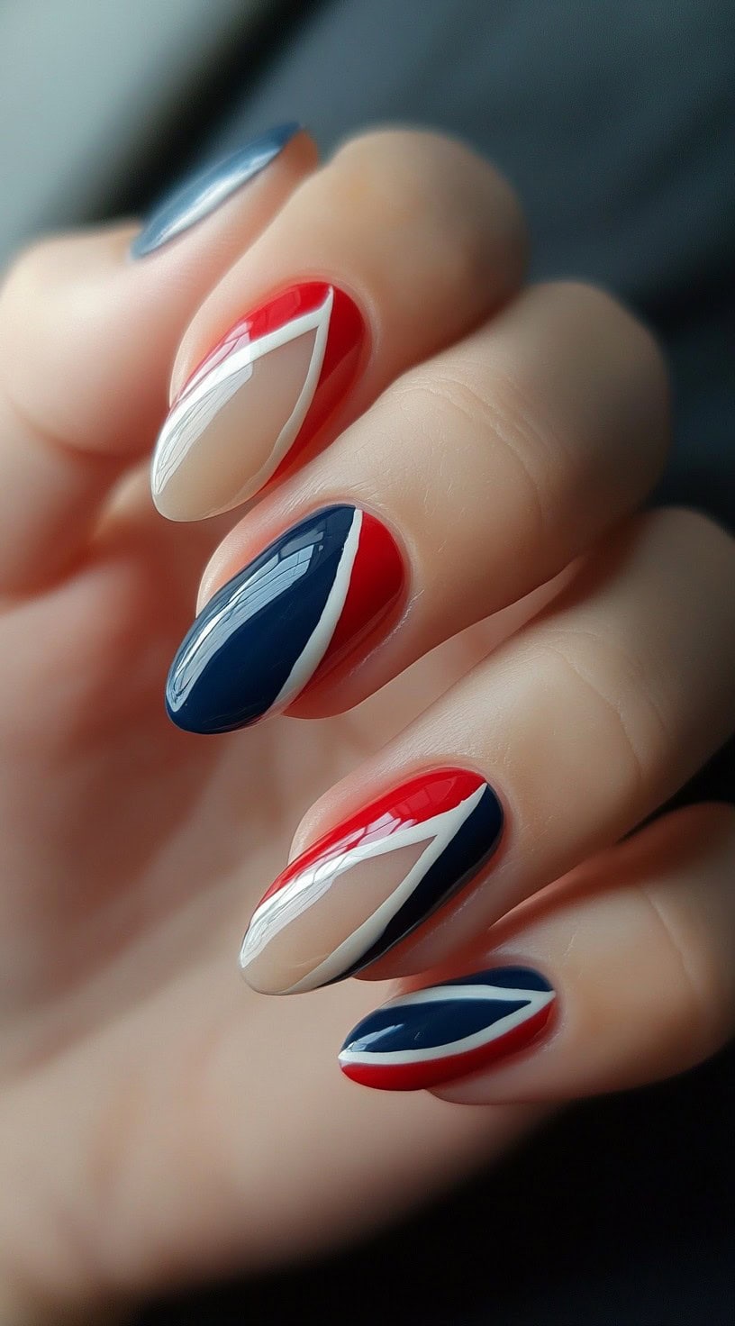 Almond-shaped nails featuring a geometric pattern in red, white, and navy with bold lines and sharp angles.