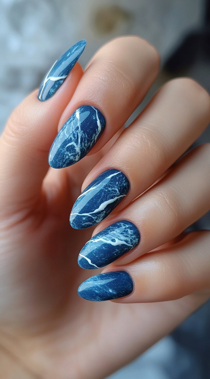 Almond-shaped nails featuring a deep navy base with white marble veins.