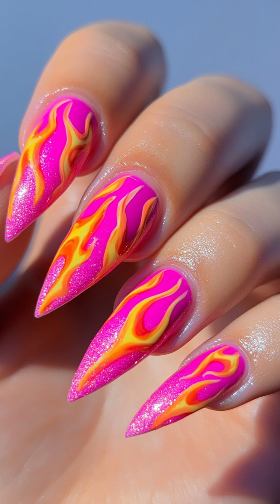 Sharp stiletto nails in hot pink with bold orange-yellow flame designs stretching up from the tips.