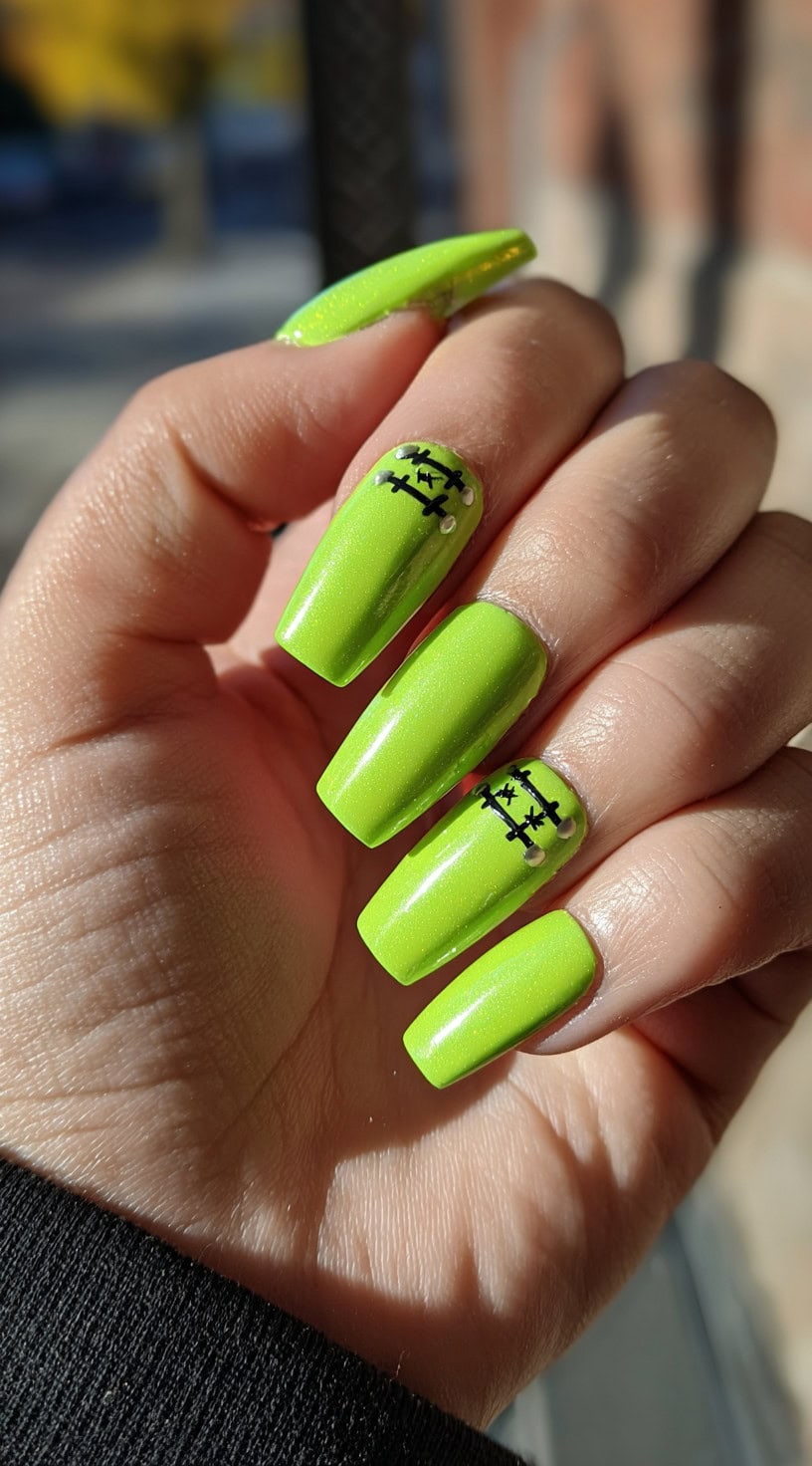 Hand with bright neon green coffin-shaped nails featuring black stitched lines and small silver stud accents near the cuticles.