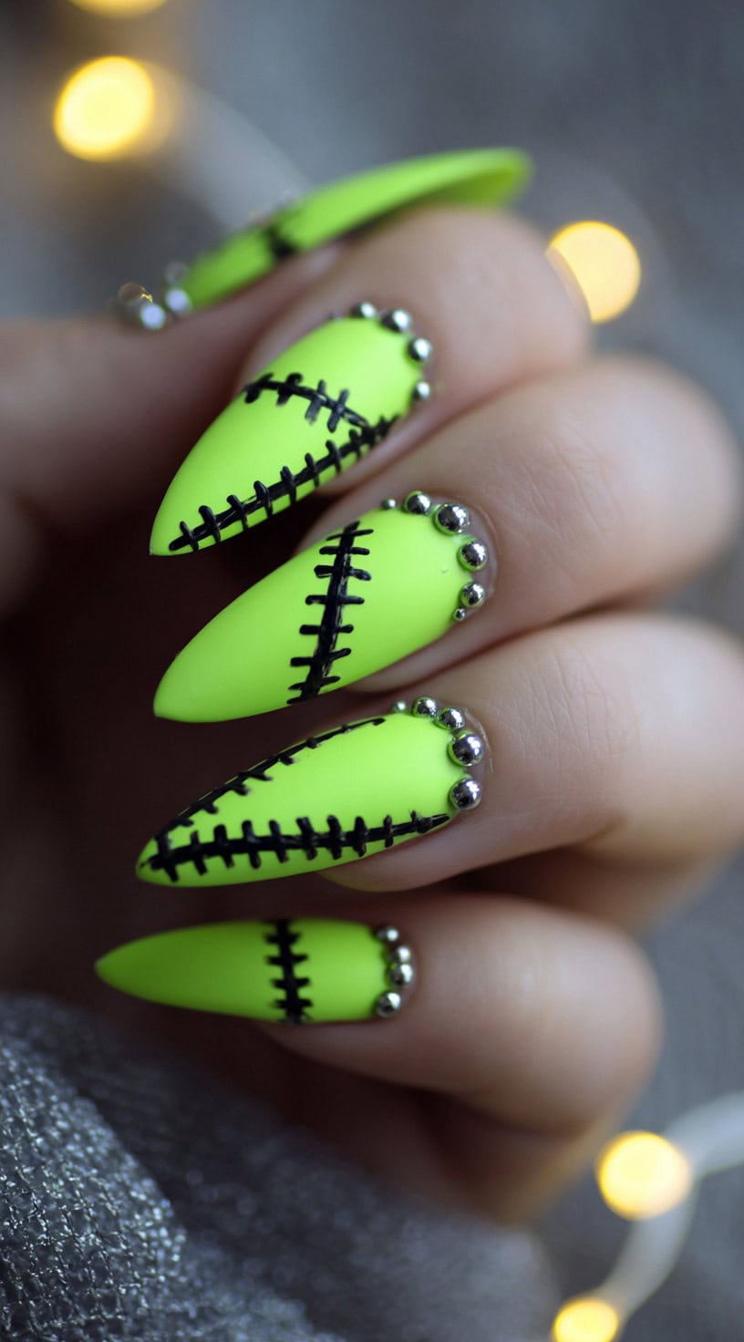 Almond-shaped matte neon green nails with thick black stitches and silver studs near the cuticles.