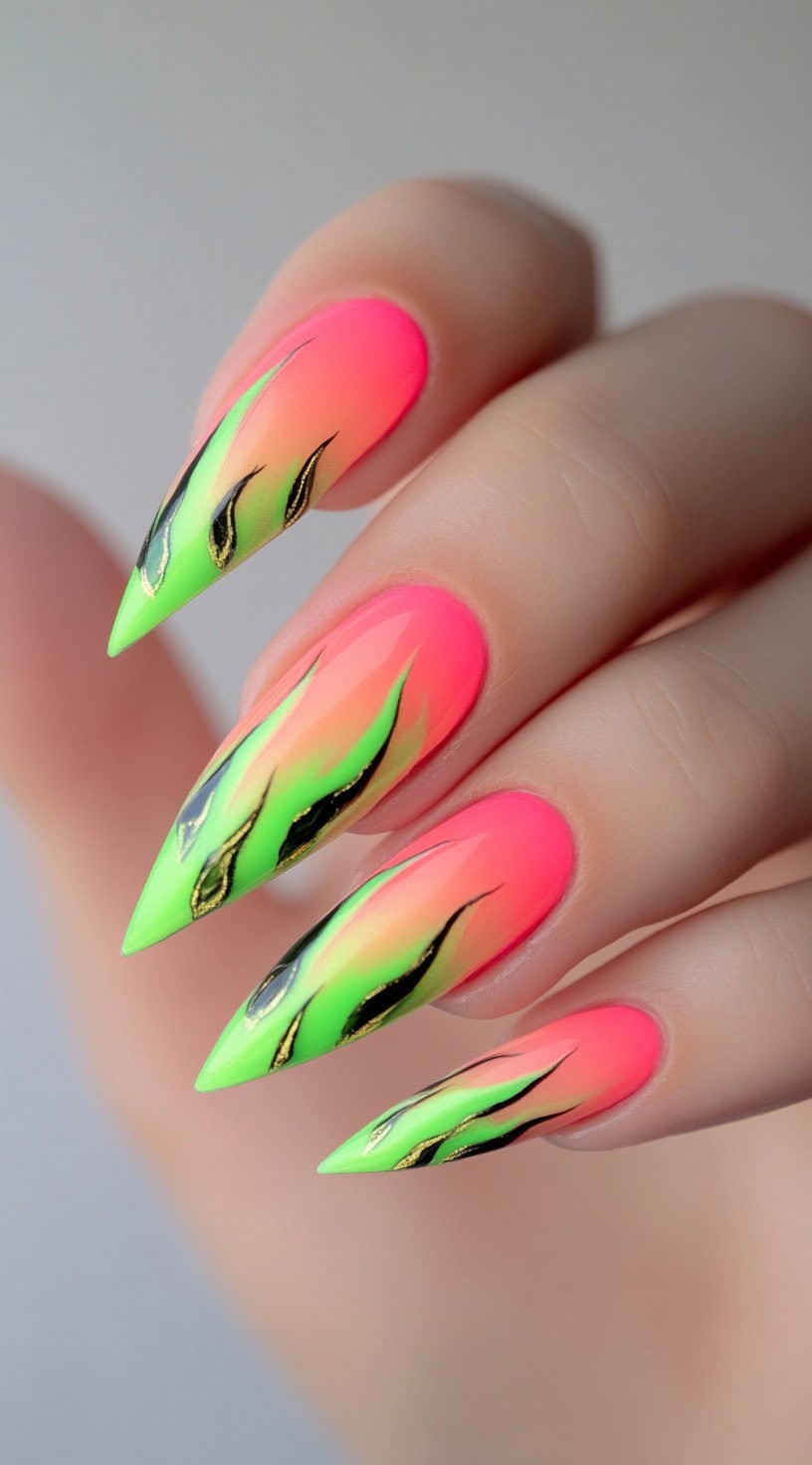 A hand with neon pink to green stiletto nails featuring black flame art over the ombre base.