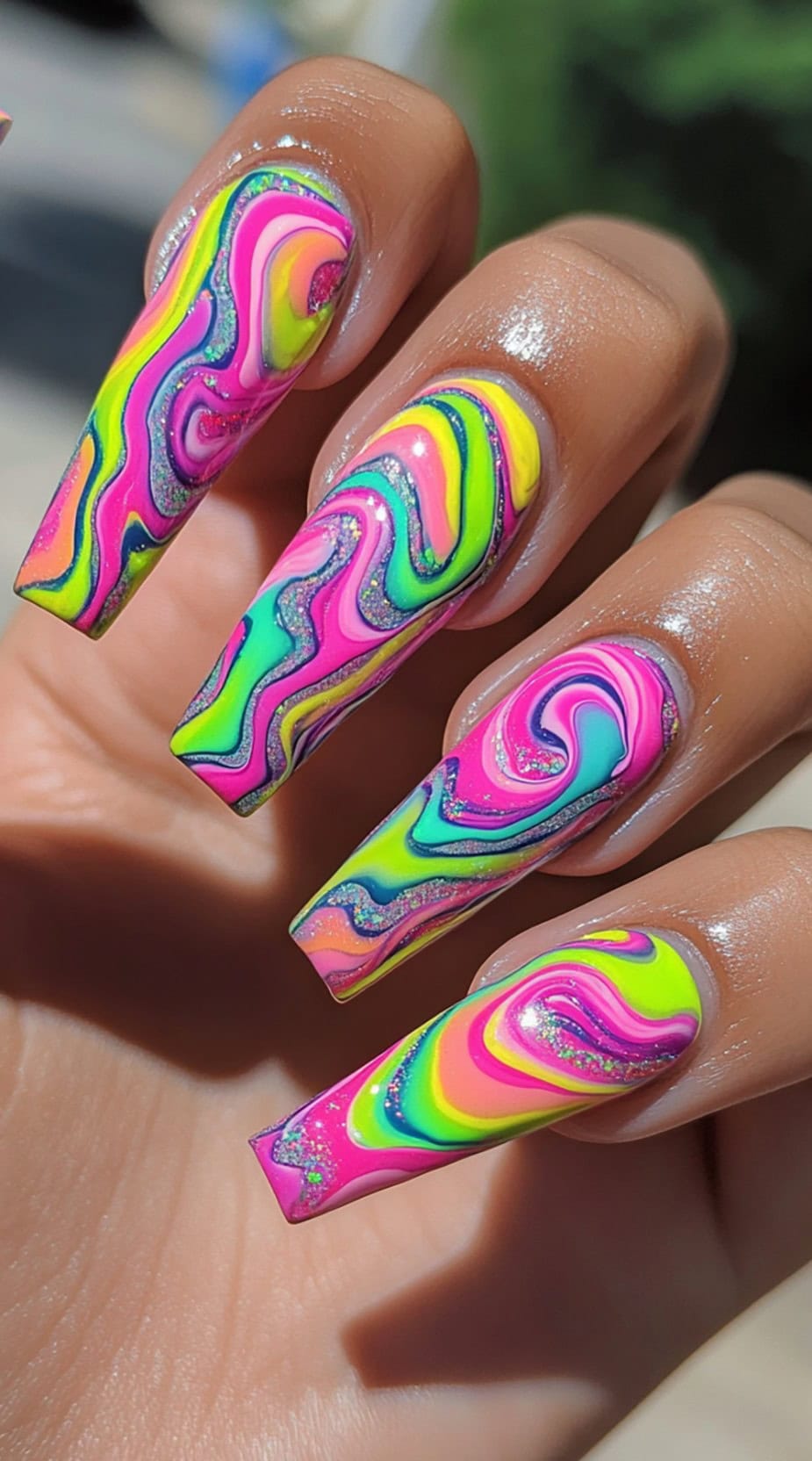 Long coffin-shaped nails with bright neon swirls in pink, yellow, green, and purple, accented with silver glitter.
