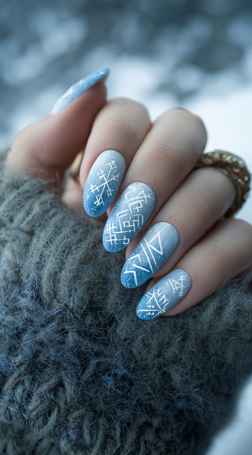 A hand with medium-length almond nails featuring a blue-to-white gradient and delicate white Viking runes.