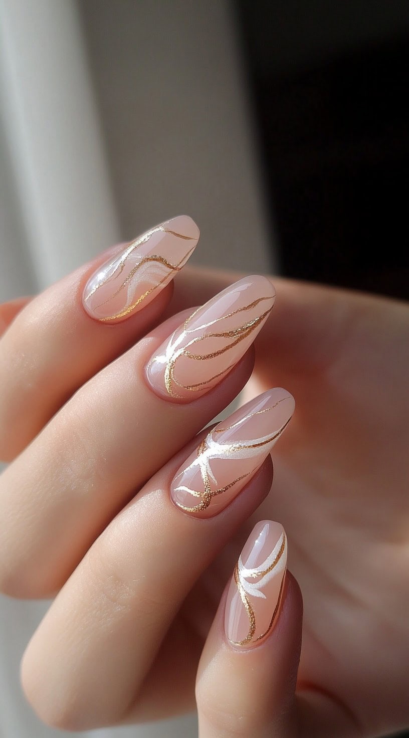 Almond-shaped nails with a sheer nude base and delicate gold abstract swirls, creating a soft and modern bridal look.